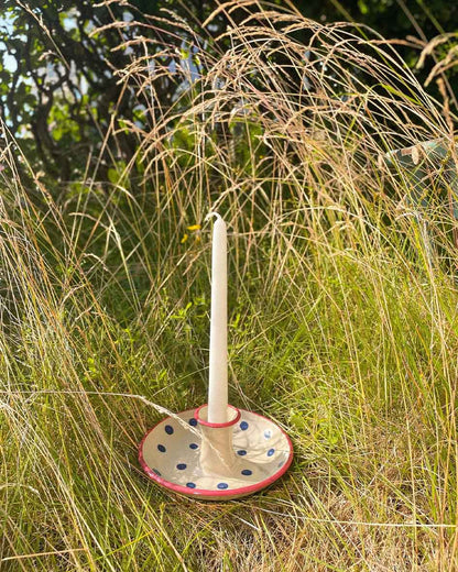 Handcrafted Spanish ceramic candle holder with blue polka dots and red rim, placed in wild grassy outdoor setting