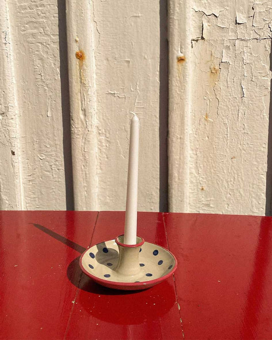 Handcrafted Spanish ceramic candle holder with blue polka dots, white candle on vibrant red surface
