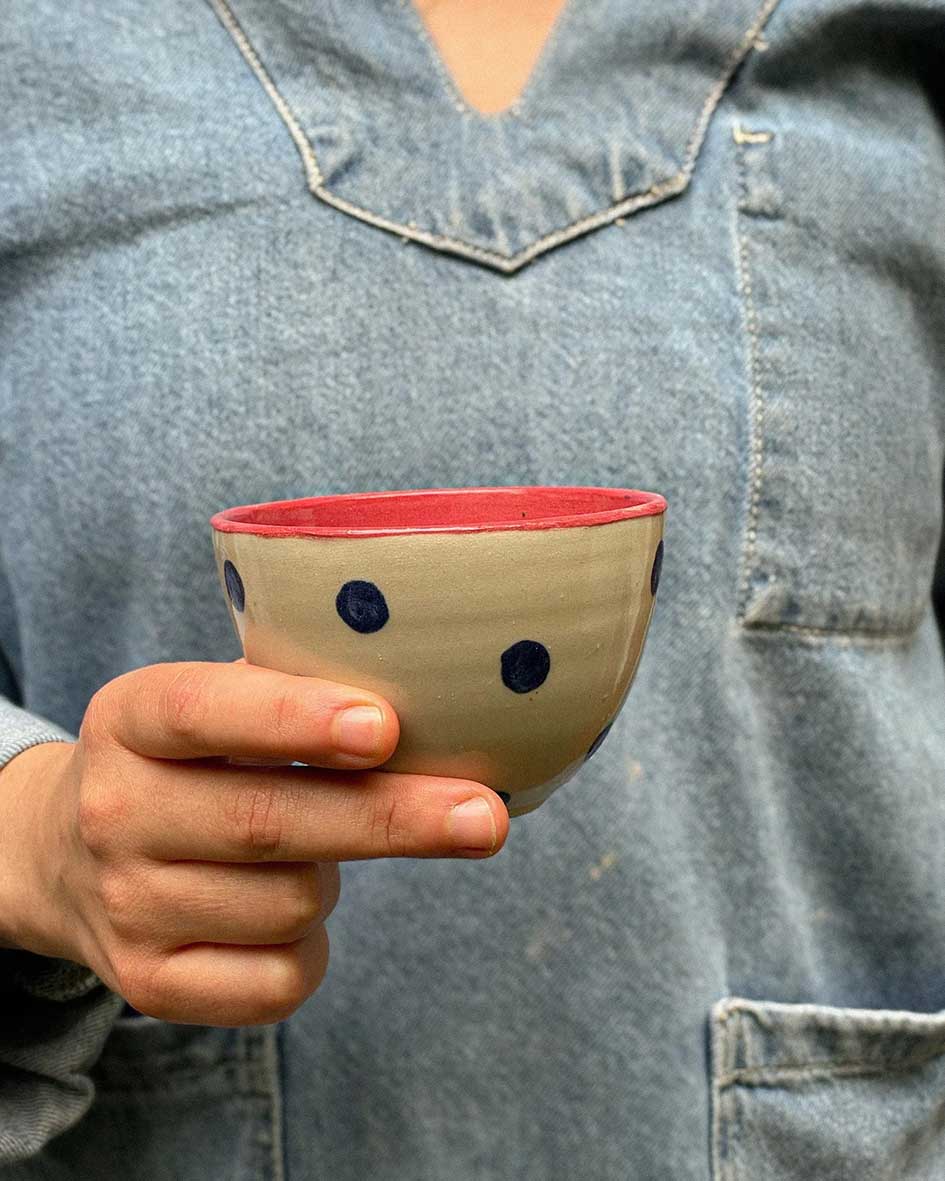 Handcrafted Spanish ceramic cappuccino cup with blue polka dots and vibrant red interior, held against denim shirt