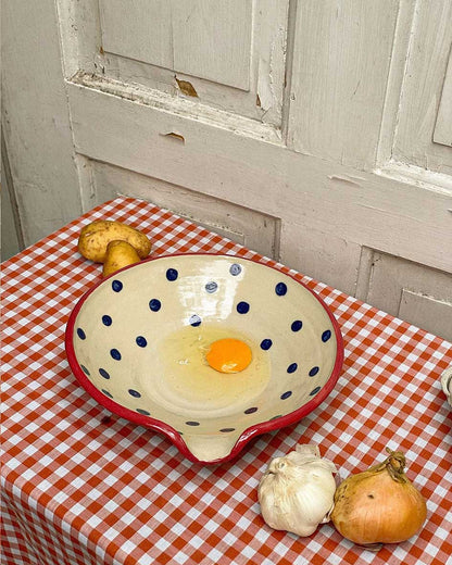 Handcrafted Spanish ceramic egg plate with blue polka dots and red rim, featuring fresh egg and rustic kitchen vegetables