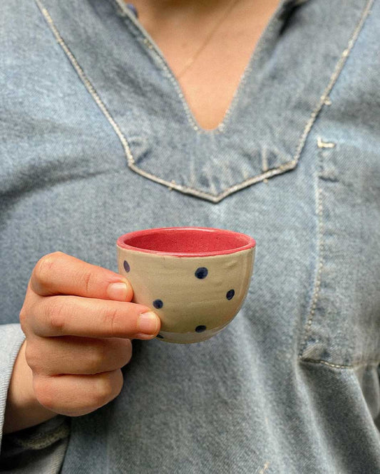 Handcrafted Spanish ceramic espresso cup with blue polka dots and red interior, held in casual lifestyle setting