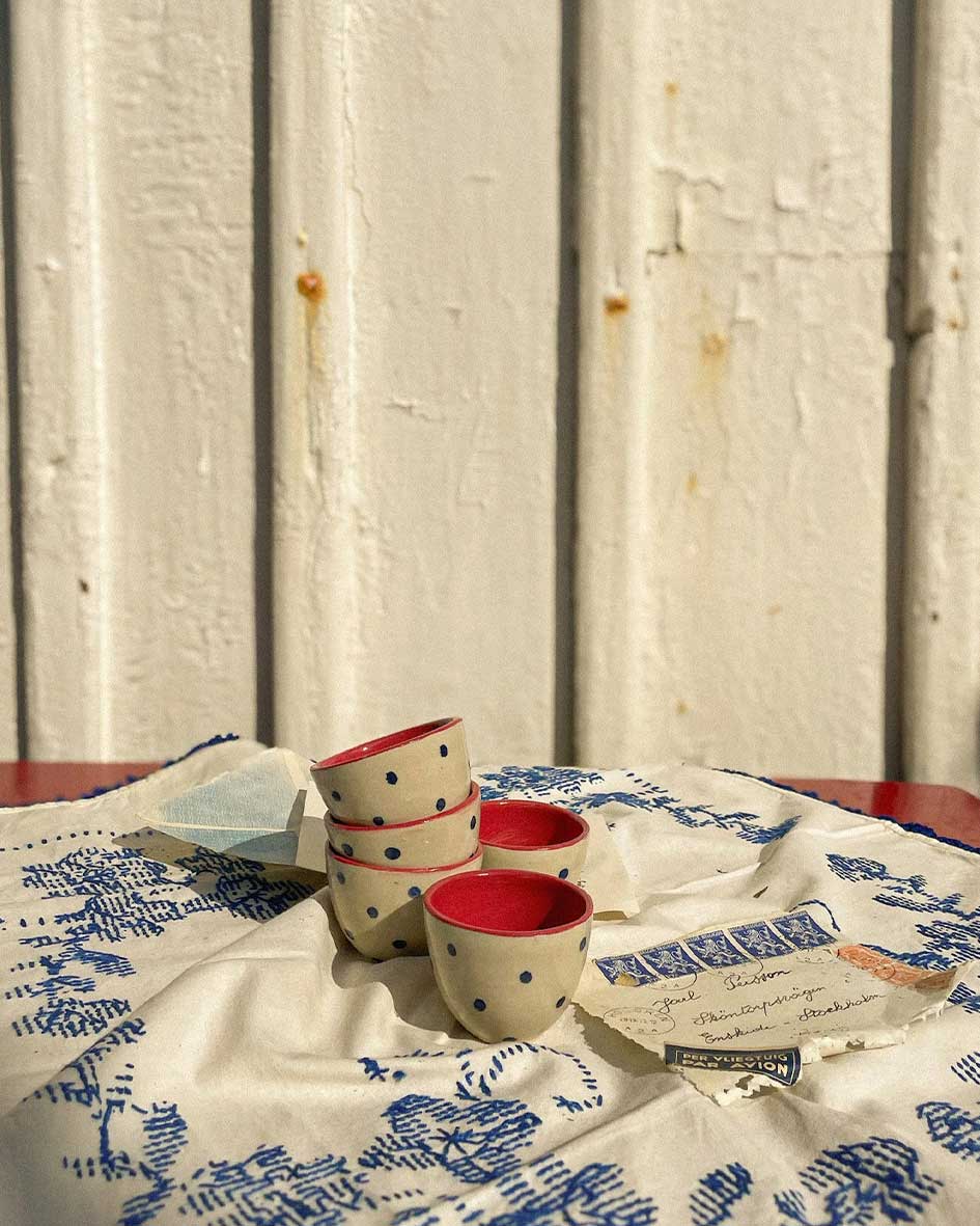Handcrafted Spanish ceramic espresso cups with blue polka dots, vibrant red interior, displayed on vintage blue-patterned textile