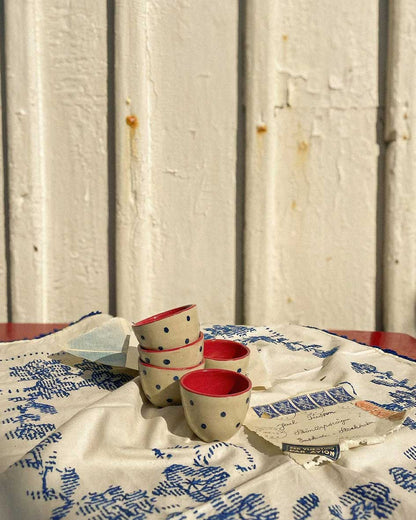 Handcrafted Spanish ceramic espresso cups with blue polka dots, vibrant red interior, displayed on vintage blue-patterned textile