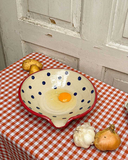Handcrafted Spanish ceramic large egg plate with blue polka dots and red rim, featuring fresh egg and rustic kitchen vegetables
