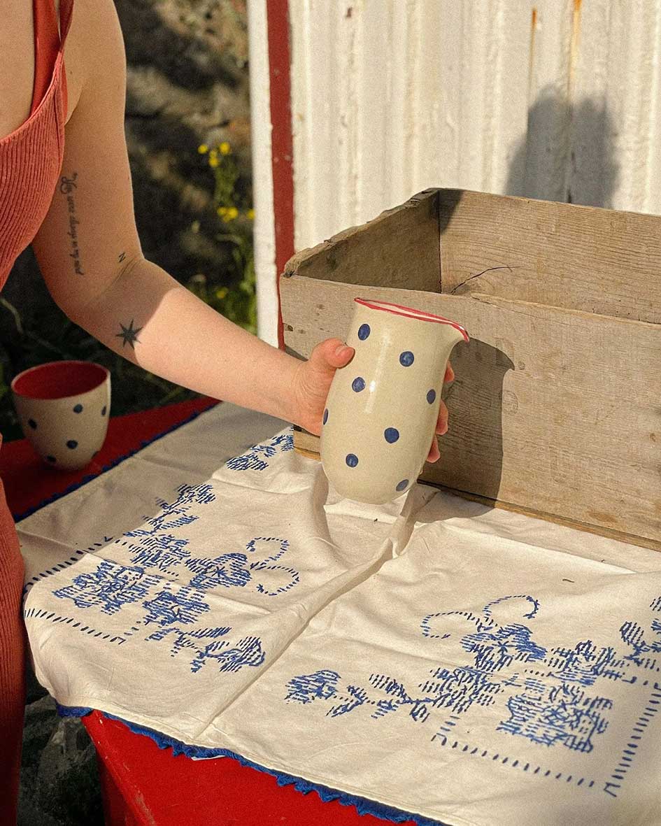 Handcrafted Spanish ceramic large milk jug with blue polka dots and red rim, pouring liquid on vintage blue-patterned textile