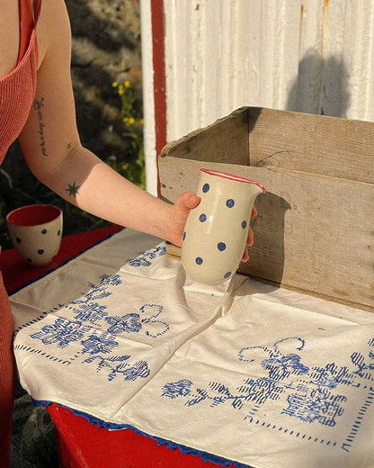 Handcrafted Spanish ceramic large milk jug with blue polka dots and red rim, pouring liquid on vintage blue-patterned textile
