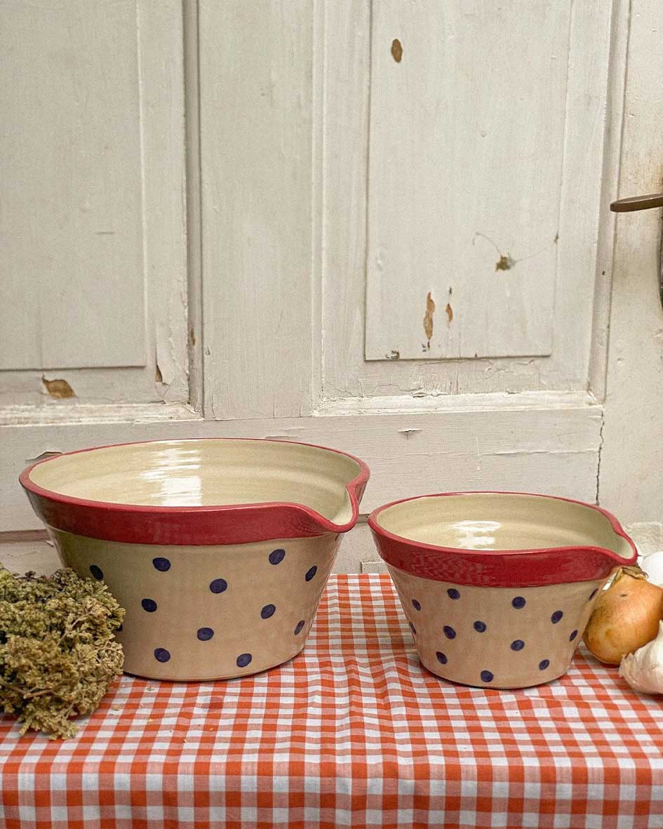 Handcrafted Spanish ceramic large mixing bowls with blue polka dots and red rims, displayed on orange gingham tablecloth with garlic and herbs