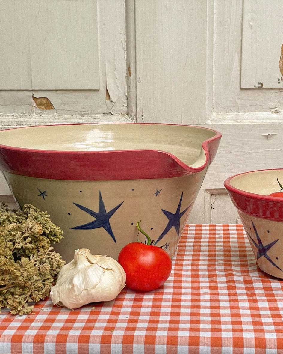 Handcrafted Spanish ceramic large mixing bowls with blue star pattern and red rim, displayed with fresh tomato and garlic on orange gingham tablecloth