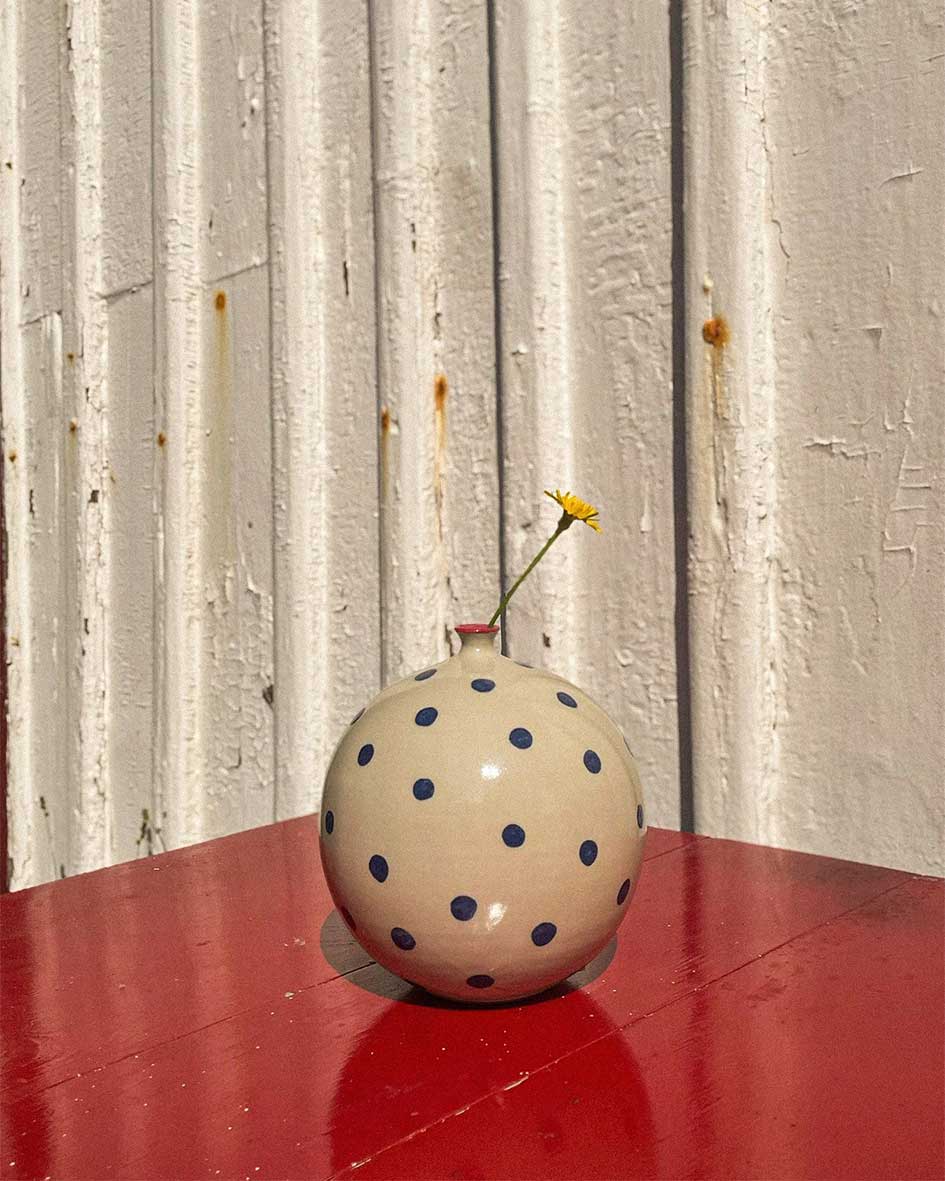 Handcrafted Spanish ceramic large vase with blue polka dots, featuring single yellow wildflower on vibrant red surface