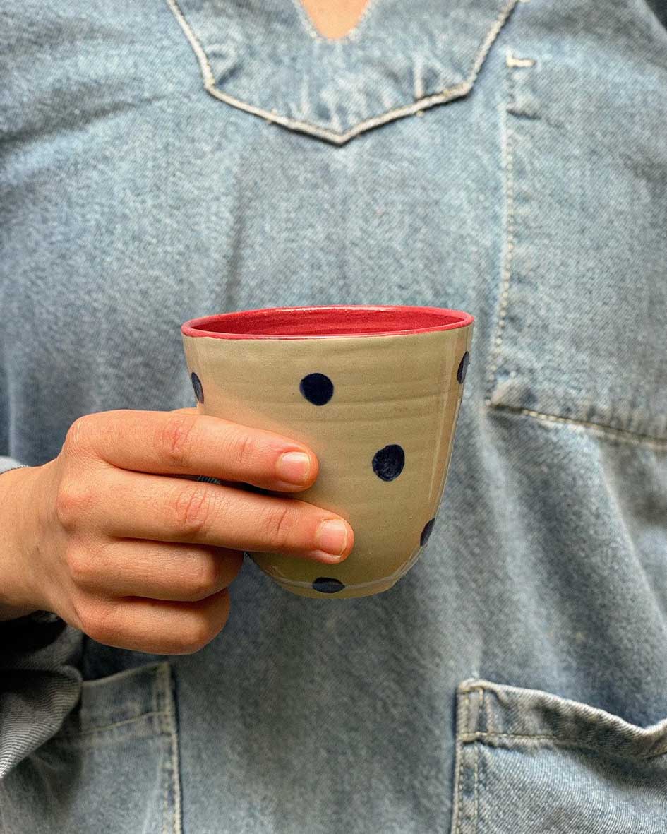 Handcrafted Spanish ceramic latte cup with blue polka dots and red interior, held against denim shirt