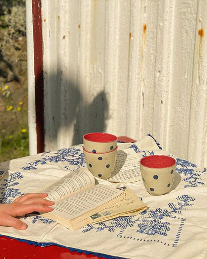 Handcrafted Spanish ceramic latte cups with blue polka dots and red interior, styled with vintage book and blue-patterned textile
