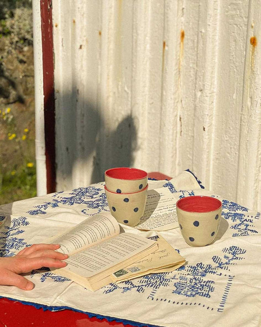 Handcrafted Spanish ceramic latte cups with blue polka dots and red interior, styled with vintage book and blue-patterned textile
