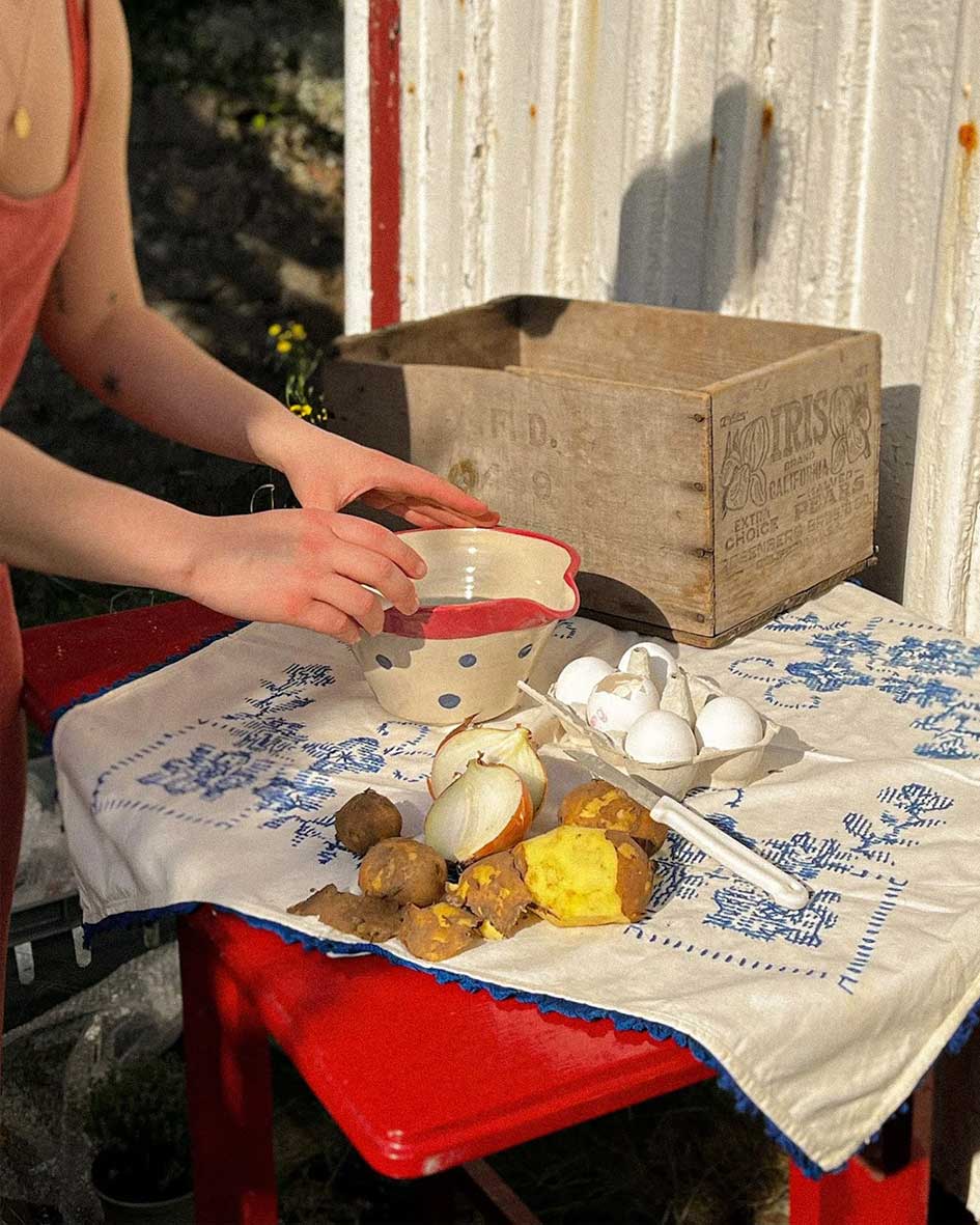 Handcrafted Spanish ceramic medium mixing bowl with blue polka dots and red rim, being used for outdoor food preparation with eggs and potatoes