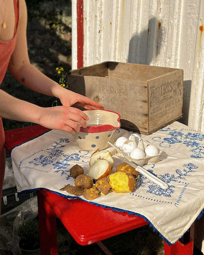 Handcrafted Spanish ceramic medium mixing bowl with blue polka dots and red rim, being used for outdoor food preparation with eggs and potatoes