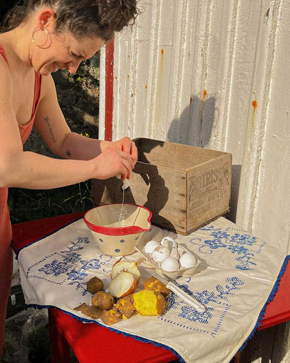 Handcrafted Spanish ceramic medium mixing bowl with blue polka dots and red rim, being used for outdoor food preparation with eggs and vegetables