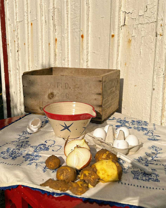 Handcrafted Spanish ceramic medium mixing bowl with blue star pattern and red rim, displayed with eggs and potatoes on vintage blue-patterned textile