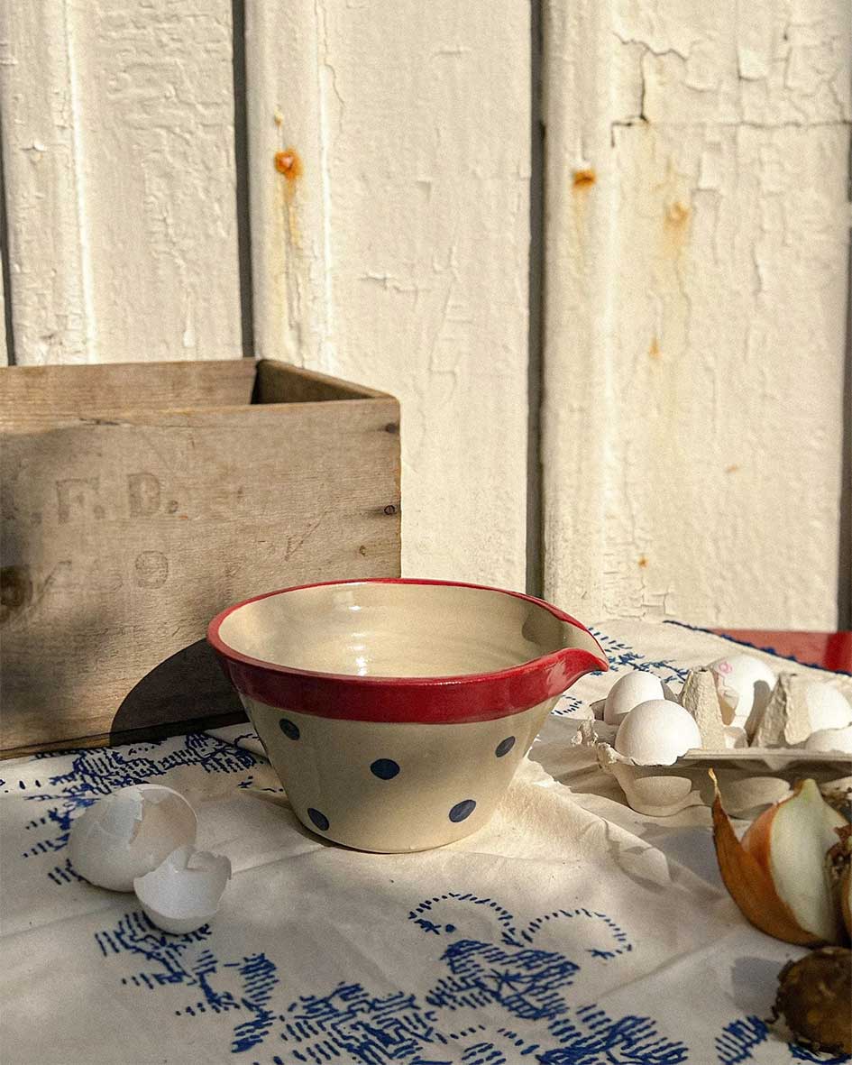 Handcrafted Spanish ceramic medium mixing bowl with blue polka dots and red rim, displayed with eggs and wooden crate