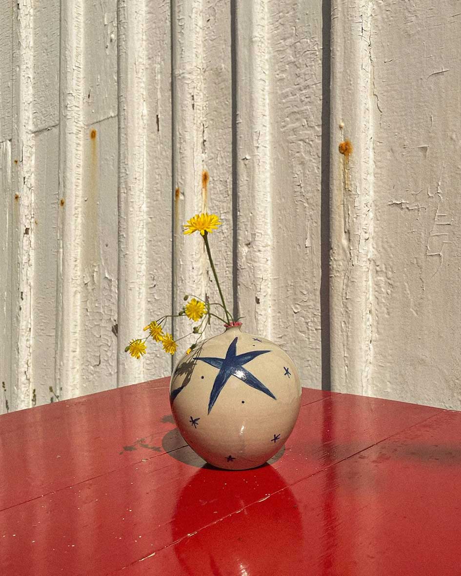 Handcrafted Spanish ceramic medium spherical vase with blue star design, adorned with yellow wildflowers on vibrant red surface