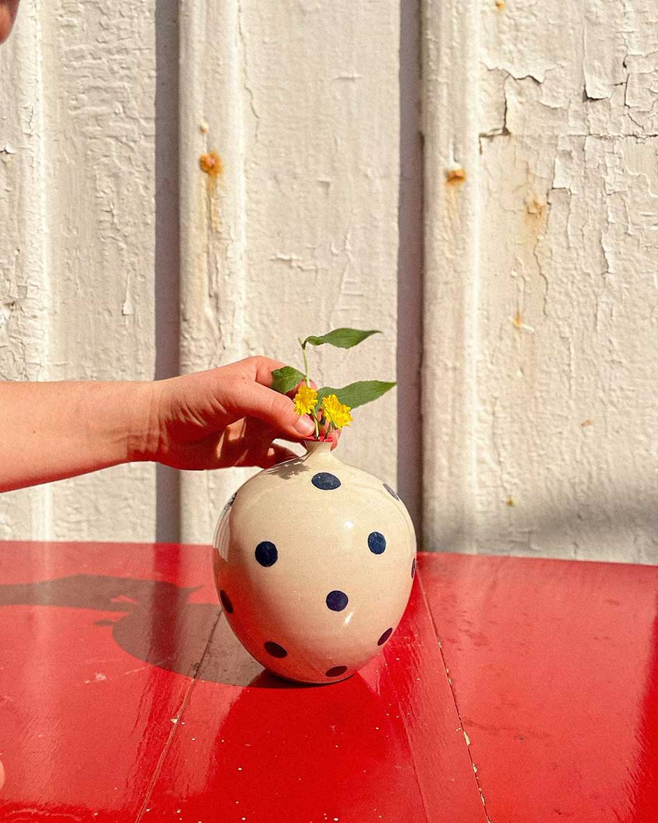 Handcrafted Spanish ceramic medium vase with blue polka dots, hand-placing small plant against white textured wall