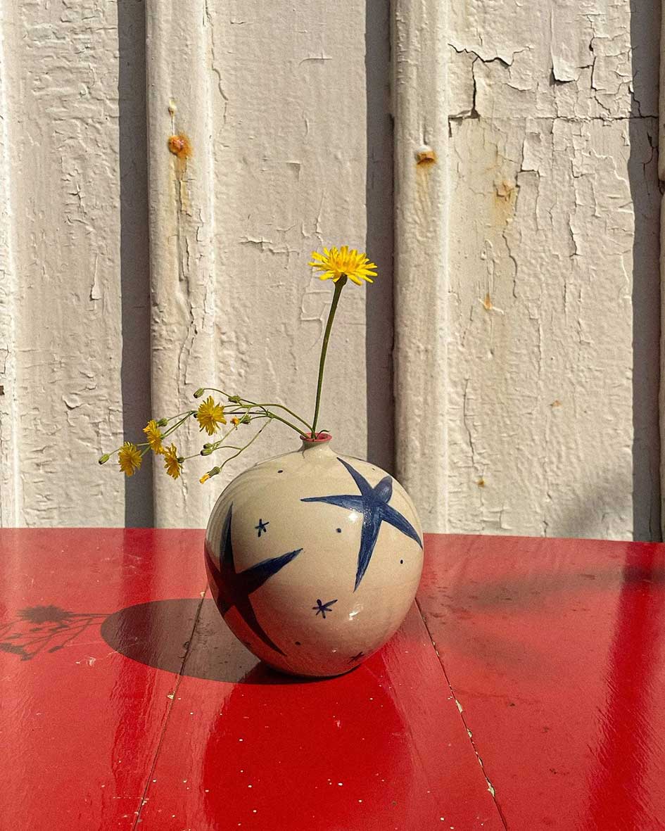 Handcrafted Spanish ceramic medium vase with blue star design, adorned with yellow wildflowers on vibrant red surface