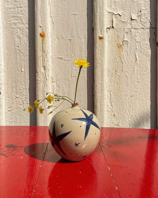 Handcrafted Spanish ceramic medium vase with blue star design, adorned with yellow wildflowers on vibrant red surface
