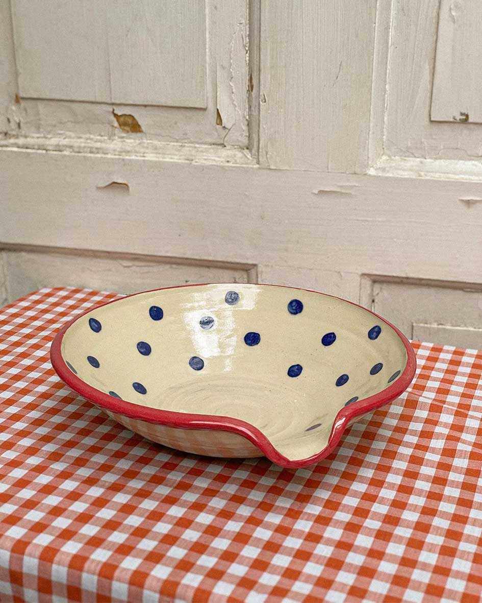 Handcrafted Spanish ceramic small egg plate with blue polka dots and red rim, displayed on orange gingham tablecloth