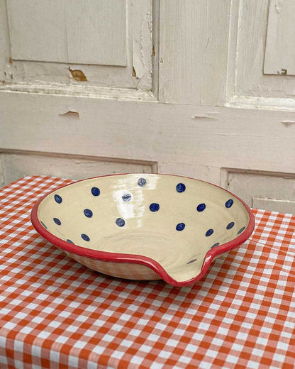 Handcrafted Spanish ceramic small egg plate with blue polka dots and red rim, displayed on orange gingham tablecloth