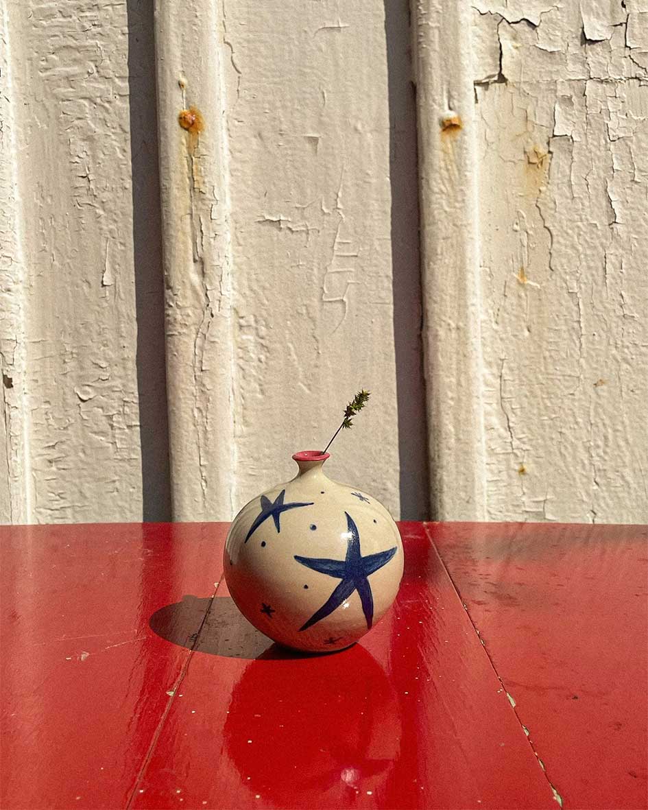 Handcrafted Spanish ceramic small vase with blue star design, featuring delicate wildflower on vibrant red surface