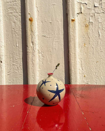 Handcrafted Spanish ceramic small vase with blue star design, featuring delicate wildflower on vibrant red surface