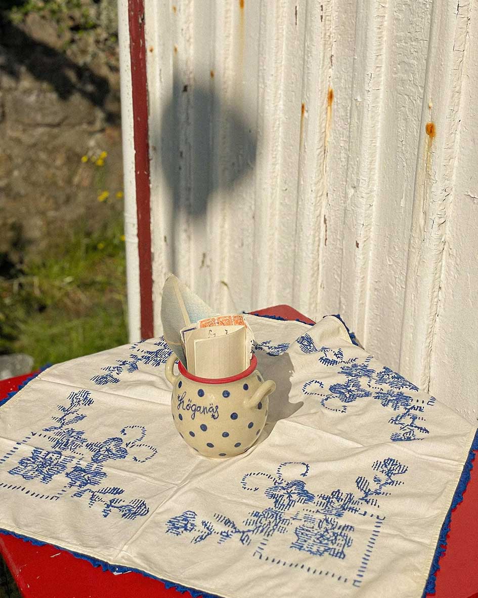 Handcrafted Spanish Hoganas ceramic pot with blue polka dots and red rim, resting on blue-patterned textile against rustic wooden wall