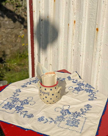 Handcrafted Spanish Hoganas ceramic pot with blue polka dots and red rim, resting on blue-patterned textile against rustic wooden wall
